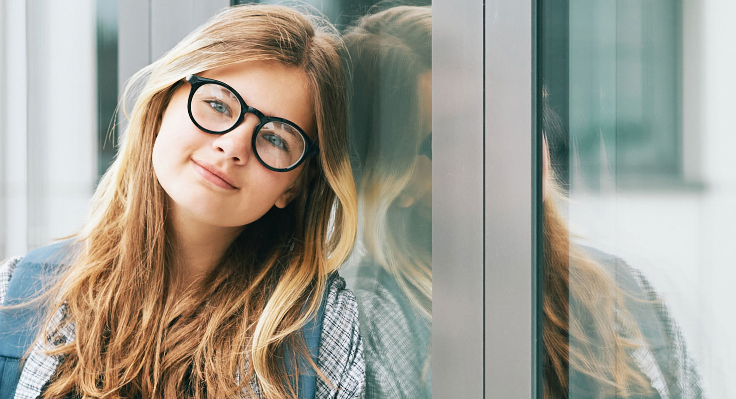 En ung tjej med glasögon står lutad mot en glasvägg.