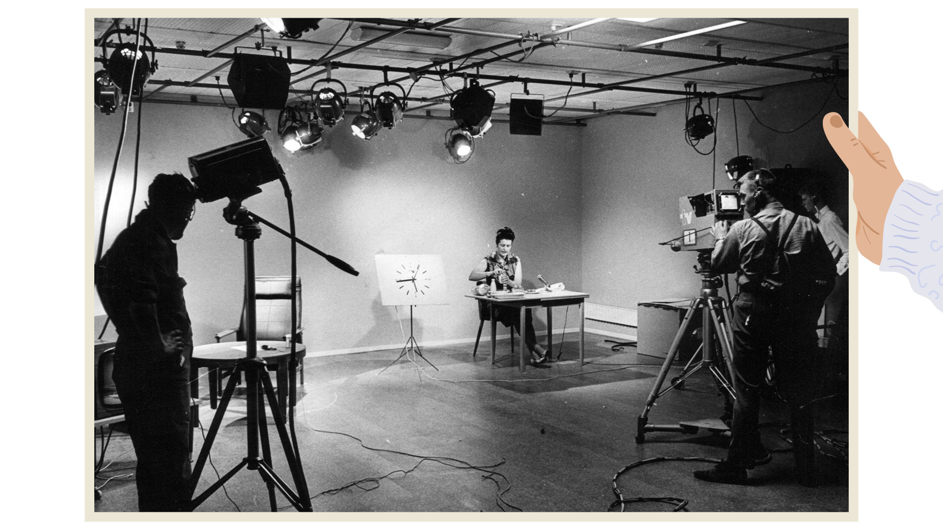 En svartvit bild som visar en TV-studio i Malmö från 1950- eller 60-talet. En kvinna sitter vid ett bord framför en klocka, medan kameramän och tekniker arbetar med belysning och kameror runtomkring. En hand pekar mot scenen för att lyfta fram detaljer.