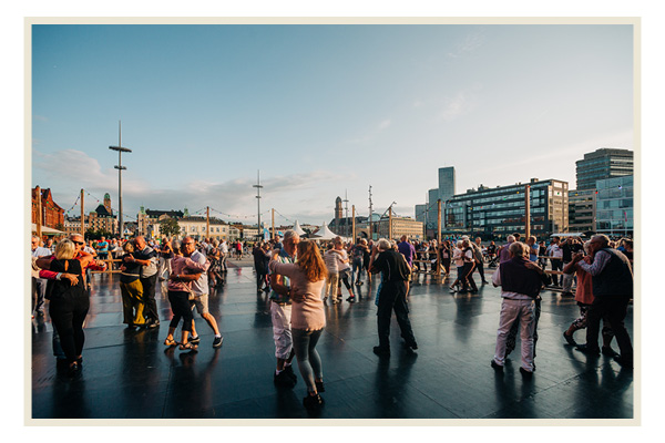 Människor dansar tango under kvällssolen vid Posthusplatsen.