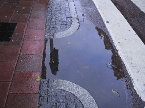 Tillgänglighetsanpassat övergångsställe där avrinningen inte fungerar. Vattnet rinner ner på övergångsstället. 