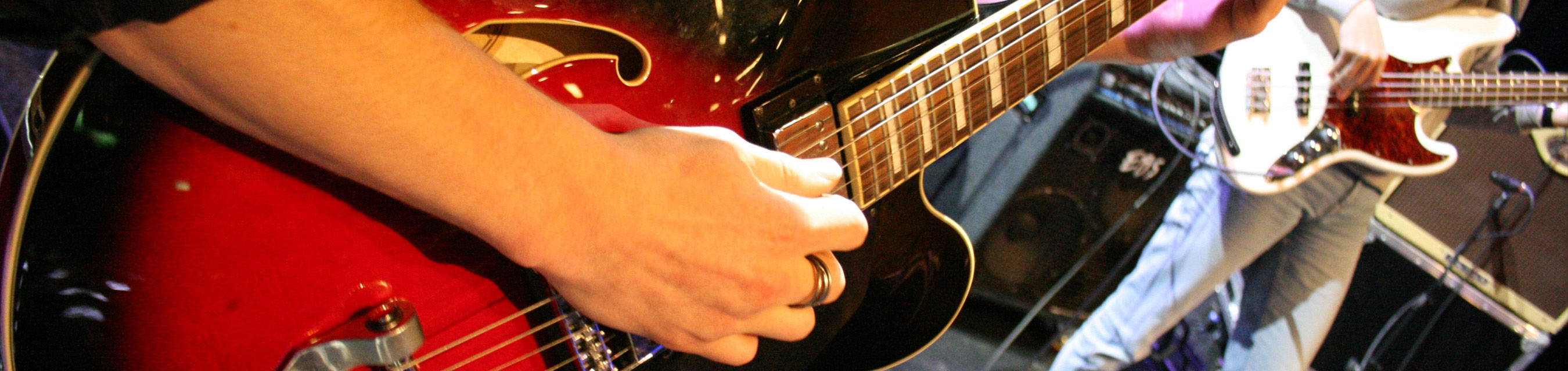 Närbild på elev med röd gitarr, i bakgrunden en annan elev med vit gitarr
