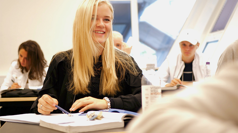 En långhårig blond elev sitter vid sin bänk och småskrattar.