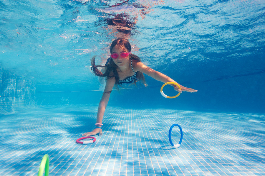 Barn dyker efter ringar under vatten i en pool