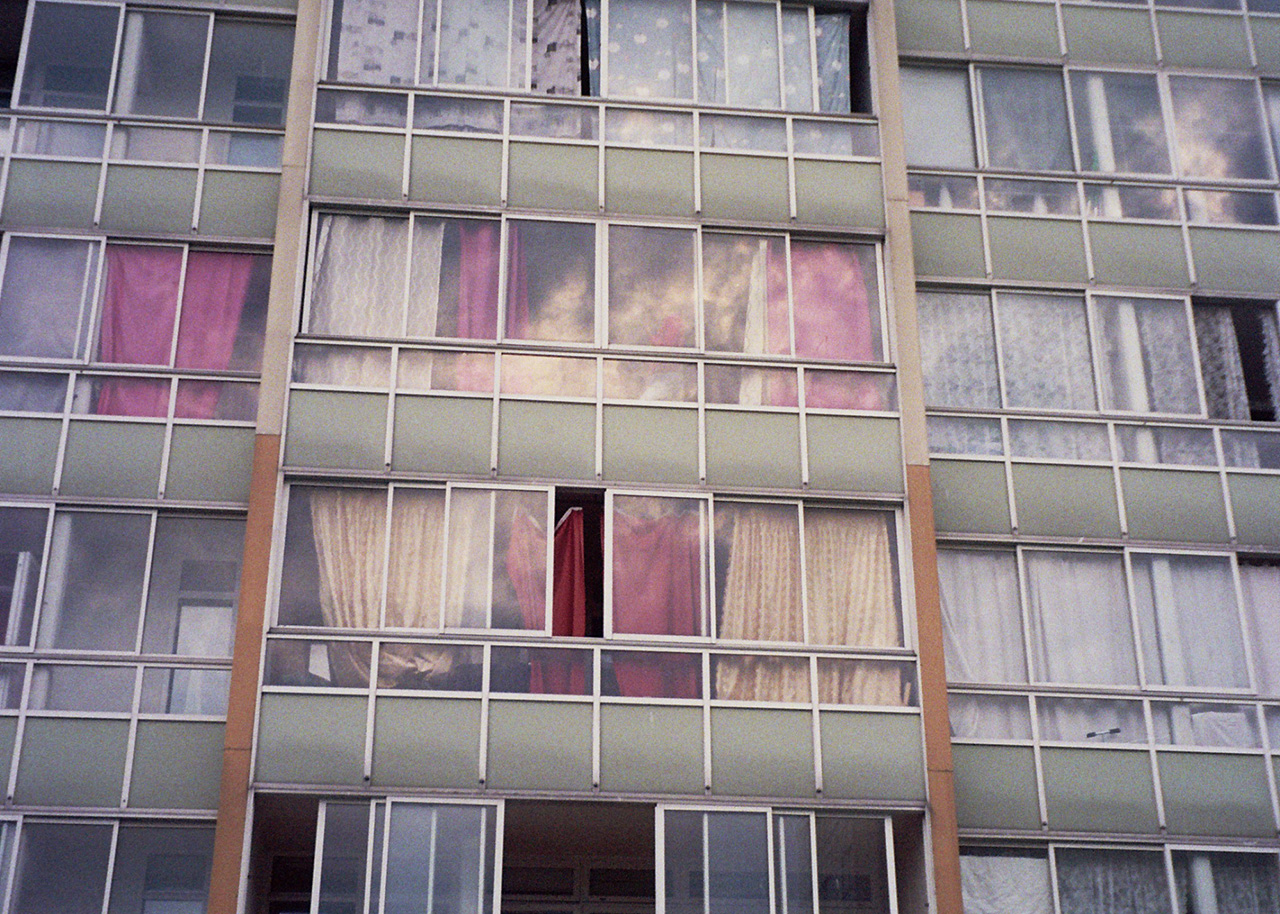 En grågrön husfasad med många fönsterpartier och inglasade balkonger på rad