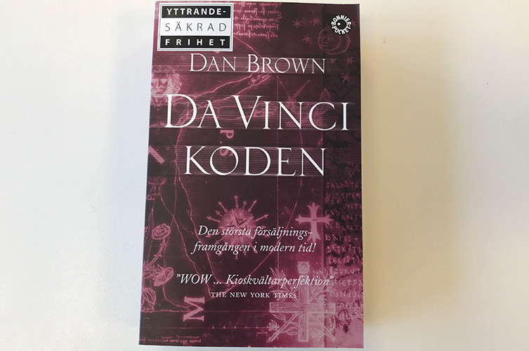 Bokomslag som föreställer Da Vinci koden. Omslaget är vinrött och lila med tecken och symboler i vitt. 
