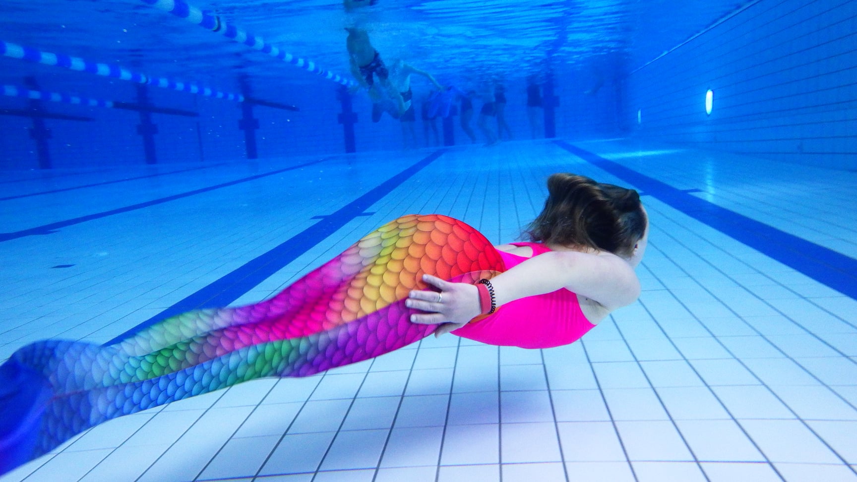 Bild under vatten i bassäng på en person som simmar med en sjöjungfrufena.