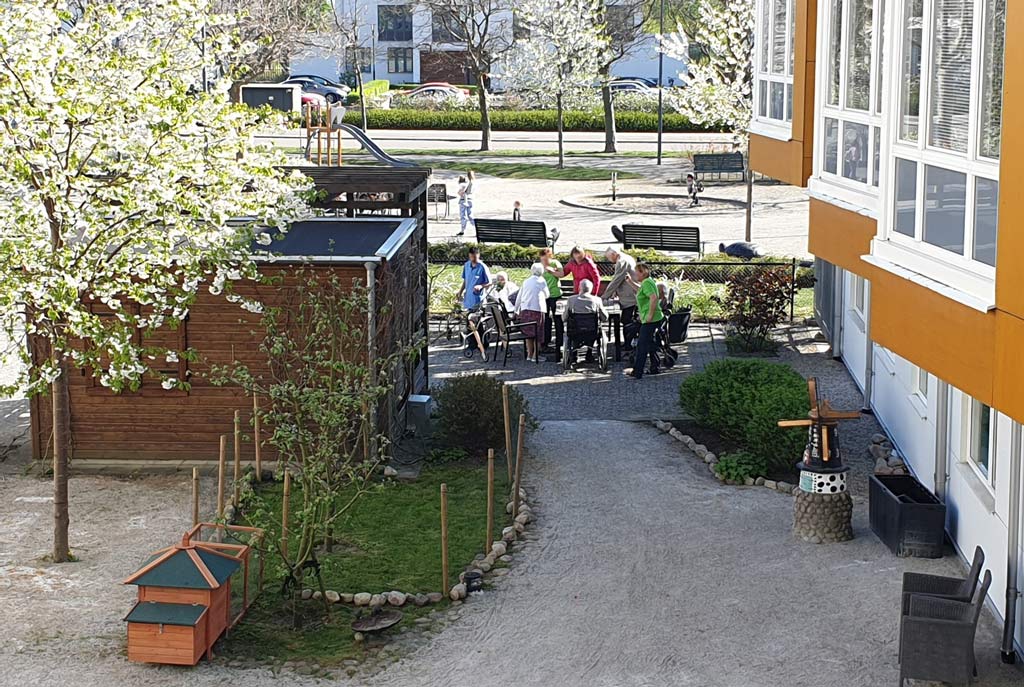 Vid uteplatsen kan man umgås i skuggan av huset med utsikt över en livfull lekplats.