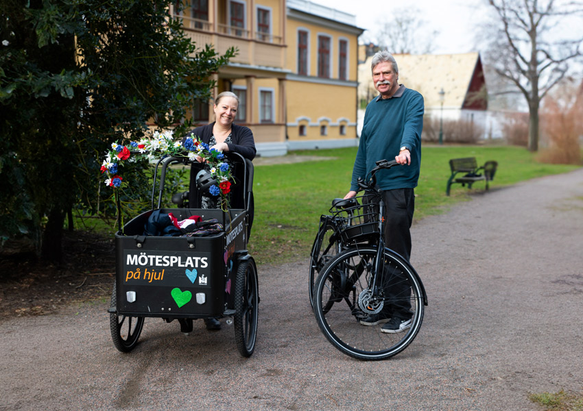 Boel och Stefan står med sina cyklar i parken och hälsar välkomna.