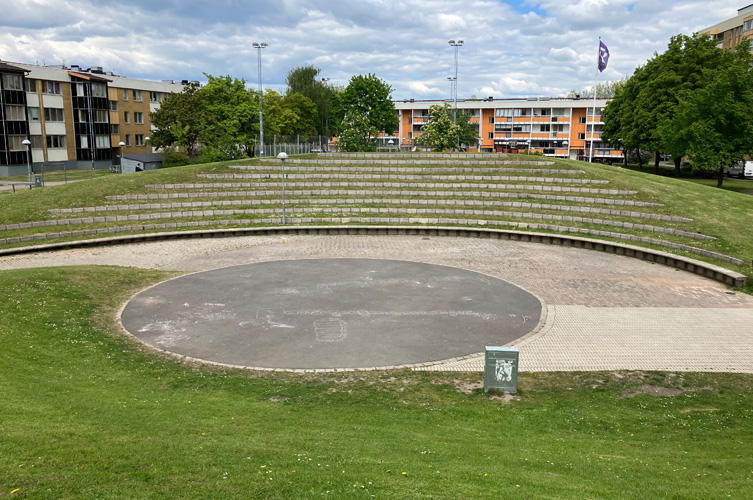 Stor amfiteater med plats till många personer på läktaren, i bakgrunden ett par flerfamiljshus byggda på 60-70-talet