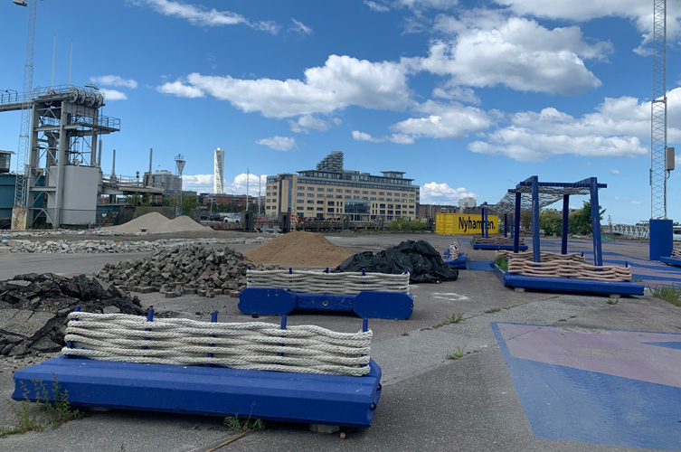 Industriområde vid hamnen, mitt i bilden ett flertal nybyggda blå bänkar av återvinningsmaterial.