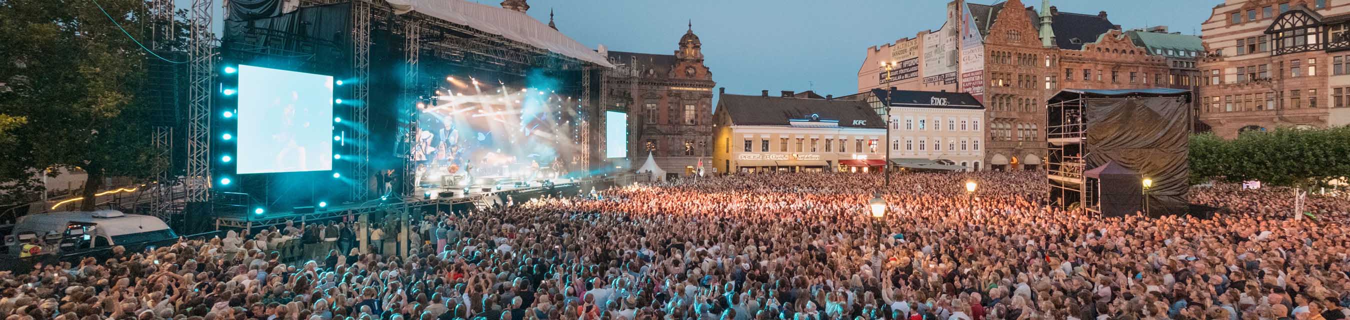 En scen där det pågår en konsert. Många människor i publiken.