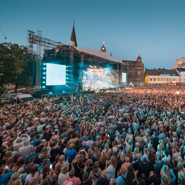 En scen där det pågår en konsert. Många människor i publiken.