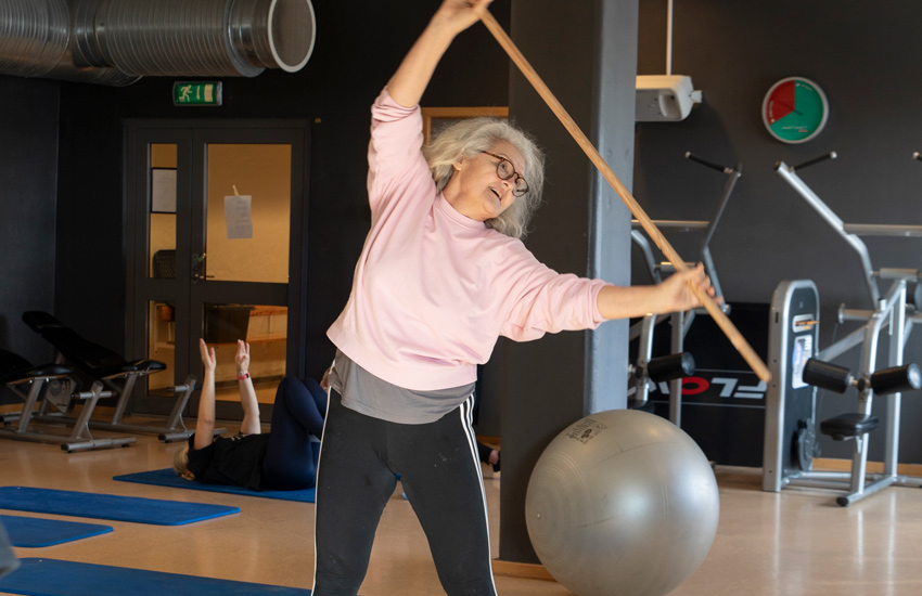 Lena har grått hår, glasögon och en rosa tröja på sig.