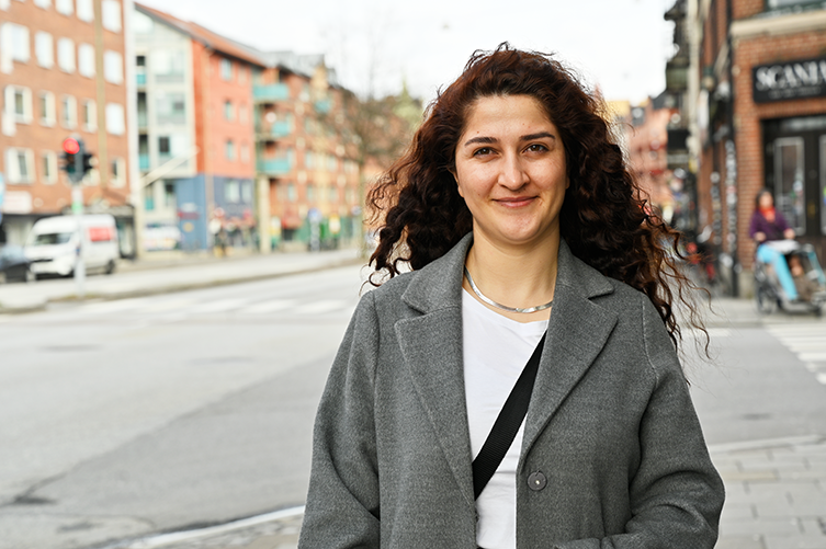 Porträttfoto på Hêlan Çiya. Çiya står på en gata, i bakgrunden syns lite trafik. 
