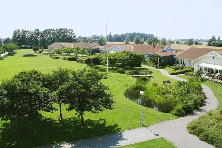 Lummig park med slingrande stigar mellan radhus och gröna gräsmattor.