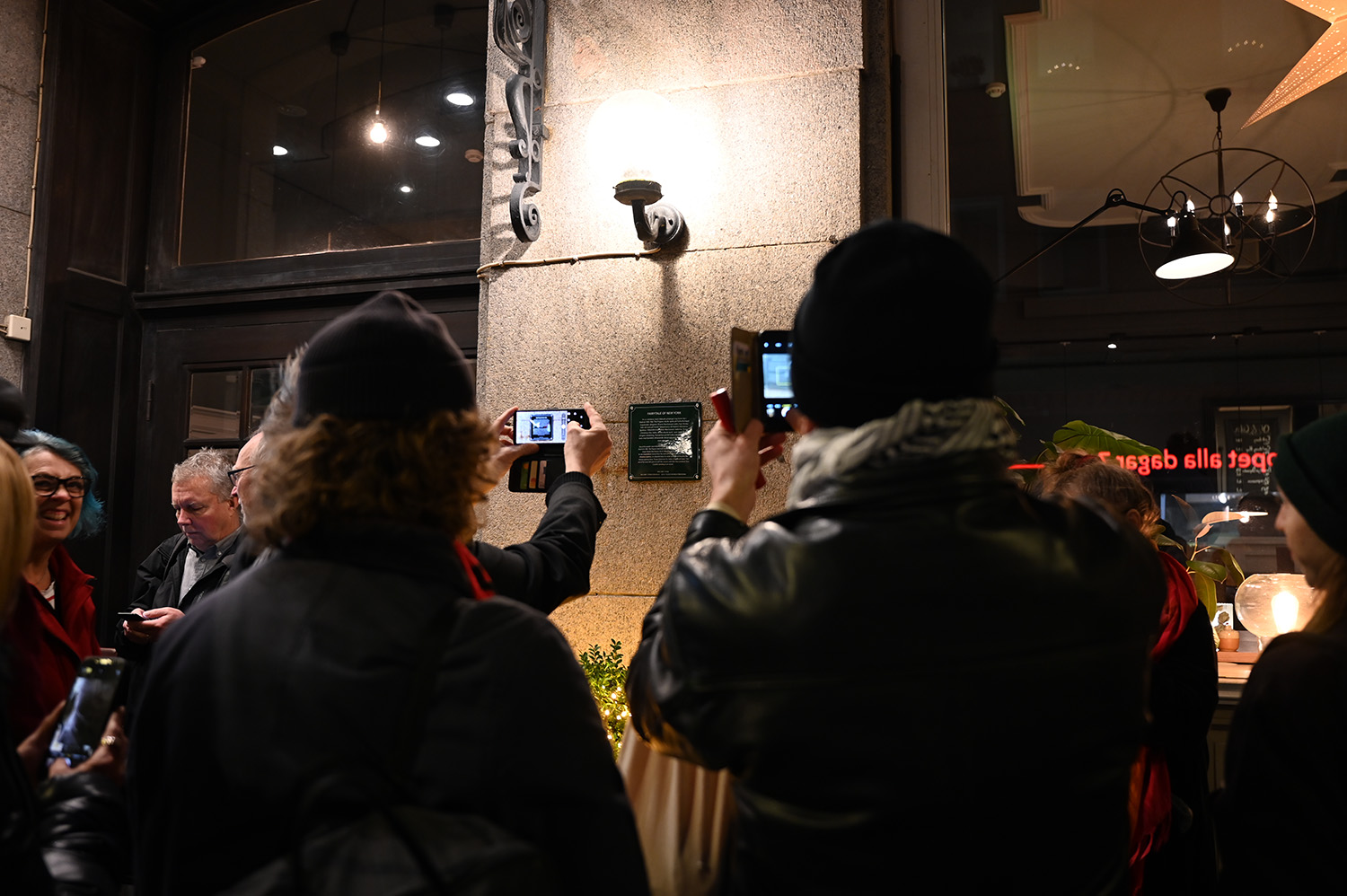 Ryggtavlorna på två personer som fotograferar den nya minnesskylten med sina mobiltelefoner.