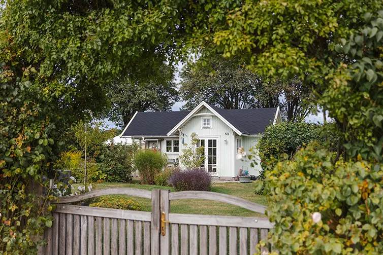 En vit kolonistuga med svart tack på en grön kolonilott. 