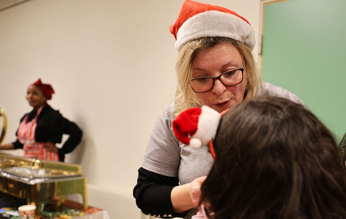 Kvinna i tomteluva pratar med ett barn med tomteluva på diadem.