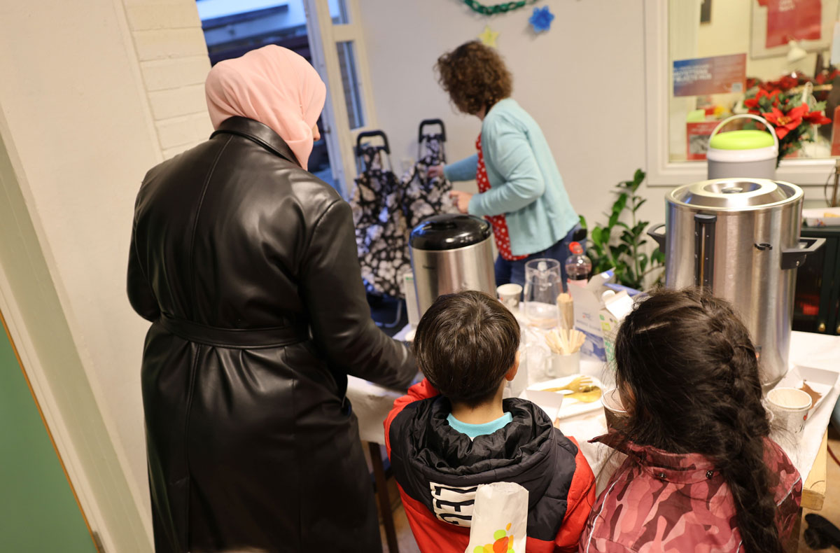 Kvinna och två barn hämtar fika hos en annan kvinna.