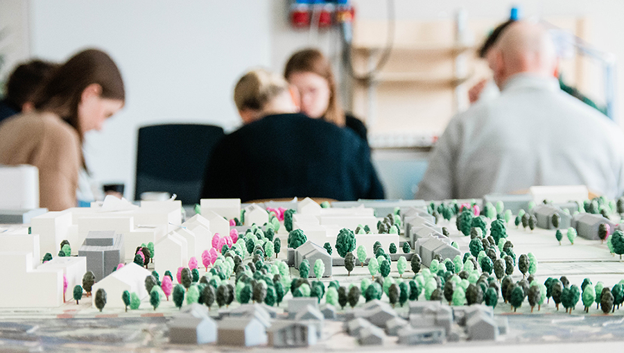 Närbild på ett modellbygge av området Sege park och människor som sitter i bakgrunden och arbetar. 