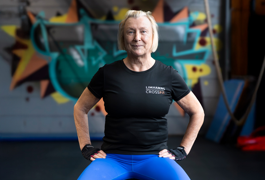 Tuula sitter på en bänk i gymmet i en kraftfull ställning med händerna i sidorna.