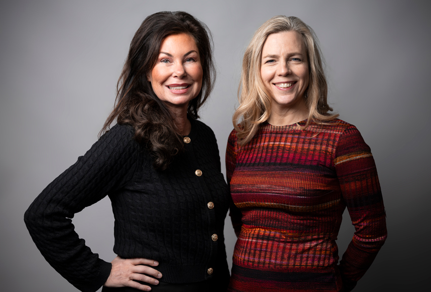 Caroline har brunt hår och en svart kofta. Jenny har blont hår och en röd tröja.