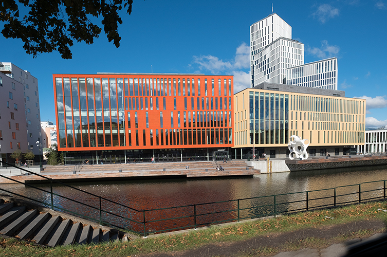 Stor ny byggnad i rött och beige. Många höga fönster. En kanal framför bygganden.