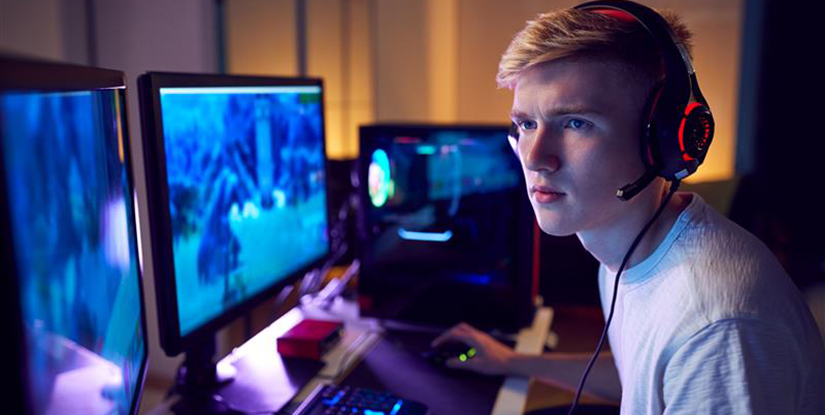 Ung kille framför en bred datorskärm spelande cybersport.