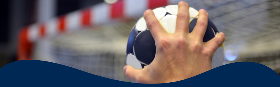 Inzoomat foto på en hand som håller en handboll framför ett handbollsmål.