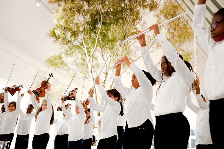 Barn i vita skjortor som alla höjer sina tvärflöjter i luften.