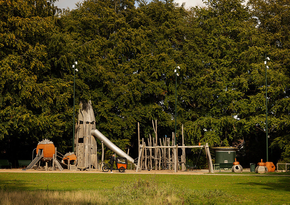 Lekplats med klätterställning och rutschbanor, i bakgrunden syns höga träd