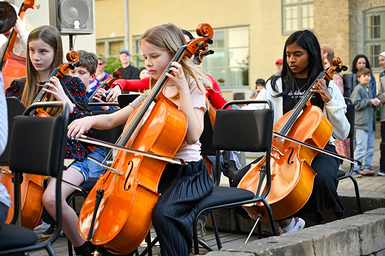 Barn som spelar i en orkester utomhus. Barnen närmast bild spelar på cello.