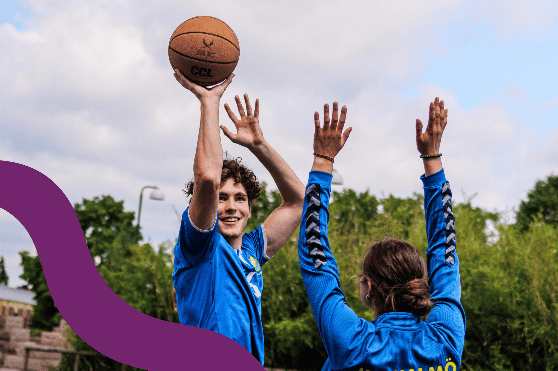Två ungdomar spelar basket utomhus.