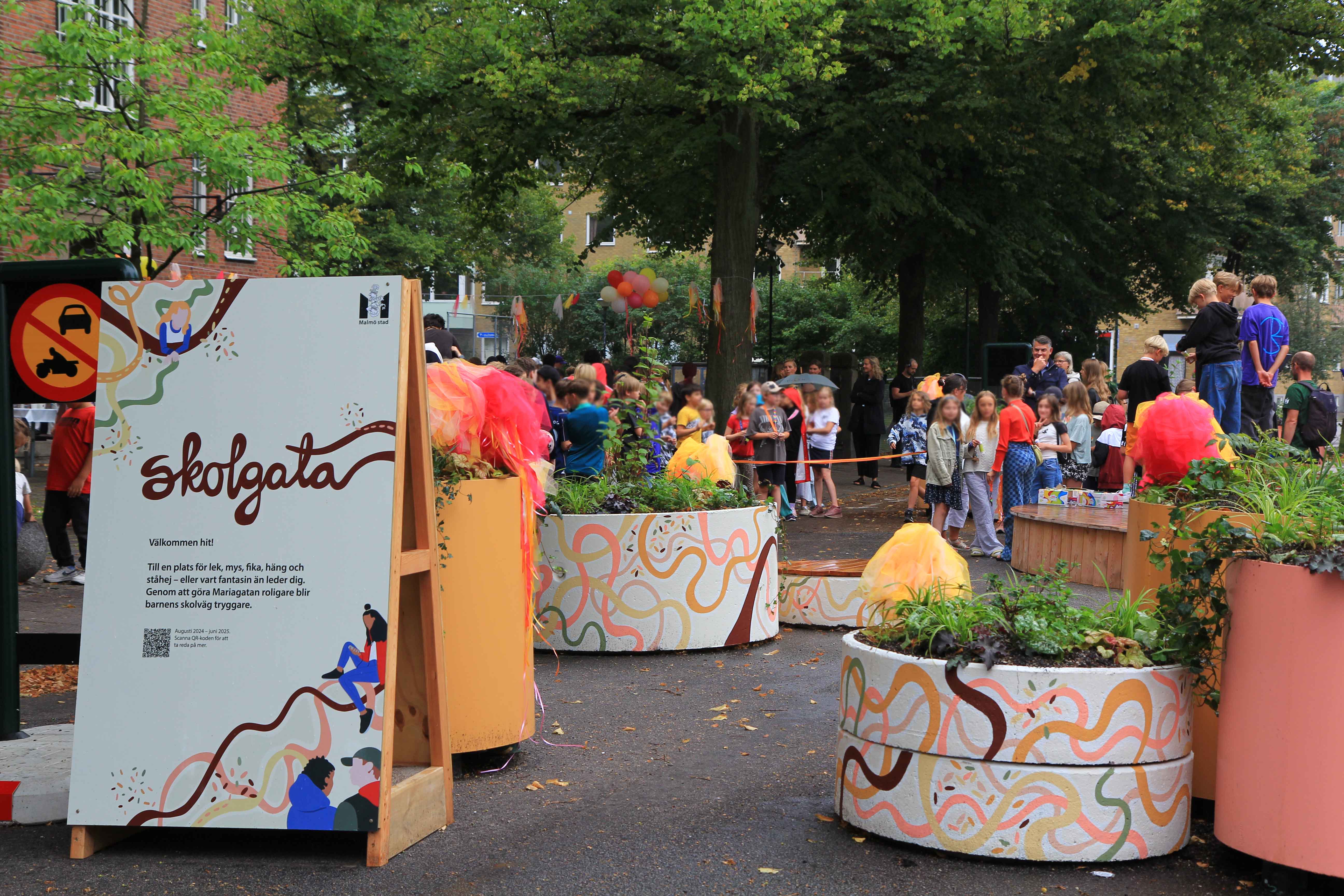 Invigningen av skolgatan på Mariagatan augusti 2024 tillsammans med eleverna från Sorgenfriskolan. I fotot syns krukor målade i olika färger, en uppsjö av skolbarn, ballonger och festlig stämning.