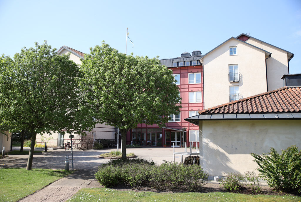 Två stora träd ramar in ett flervåningshus i vitt och
rött.
