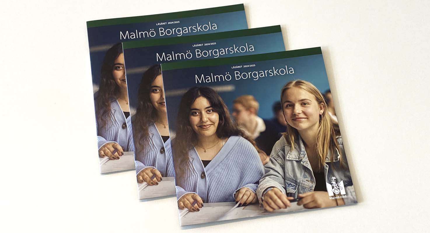 Tre exemplar på en tryckt katalog ligger staplade på en ljusfärgad yta. På katalogens omslag syns några glada elever i klassrumsmiljö.