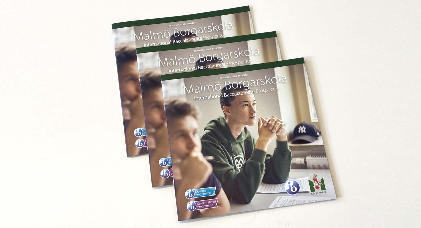 Three copies of a printed booklet lie in a pile on a light-coloured surface. On the cover, a photograph shows two students seated next to one another in a classroom setting.