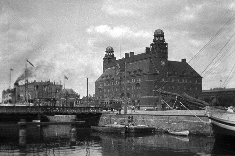 Äldre fotografi på Posthuset, en mycket ståtlig tegelbyggnad med två torn. Framför byggnaden ligger en kanal.