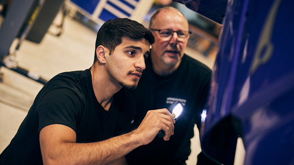 Lärare och elev lyser med en lampa mot en lastbilshuv