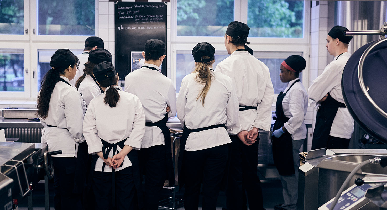 En grupp
elever på restaurang- och livsmedelsprogrammet står runt sin lärare och tittar
på vad hen gör.
