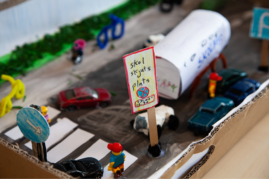 Modell i kartong med olika fordon och bland annat en skylt där det står skolskjuts-plats