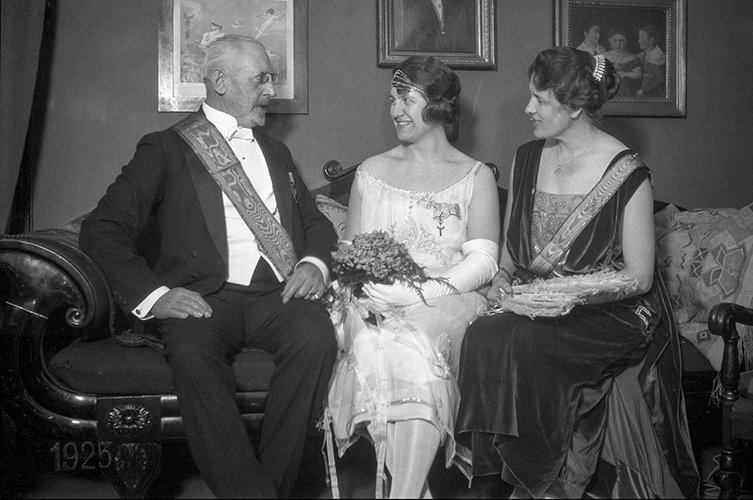 Äldre fotografi på en man och två kvinnor sittandes i en soffa, alla tre är mycket välklädda.