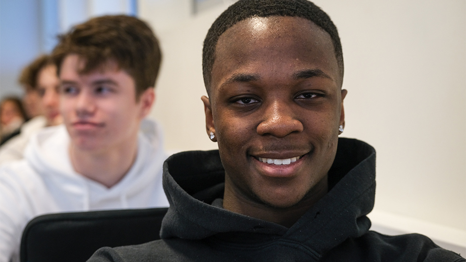 En mörk kille i närbild, suddig kompis i bakgrunden.