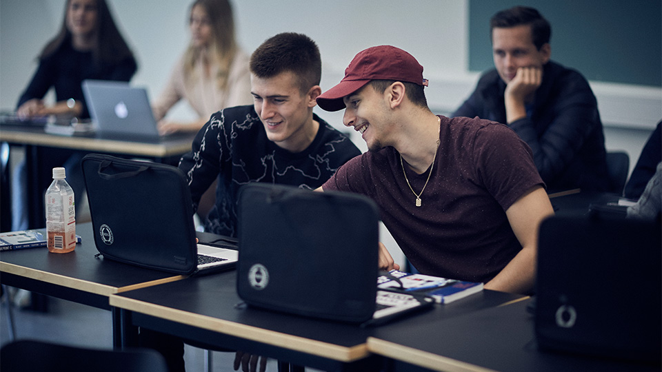 Två killar sitter vid sina bänkar, samtalar med varandra och småskrattar.