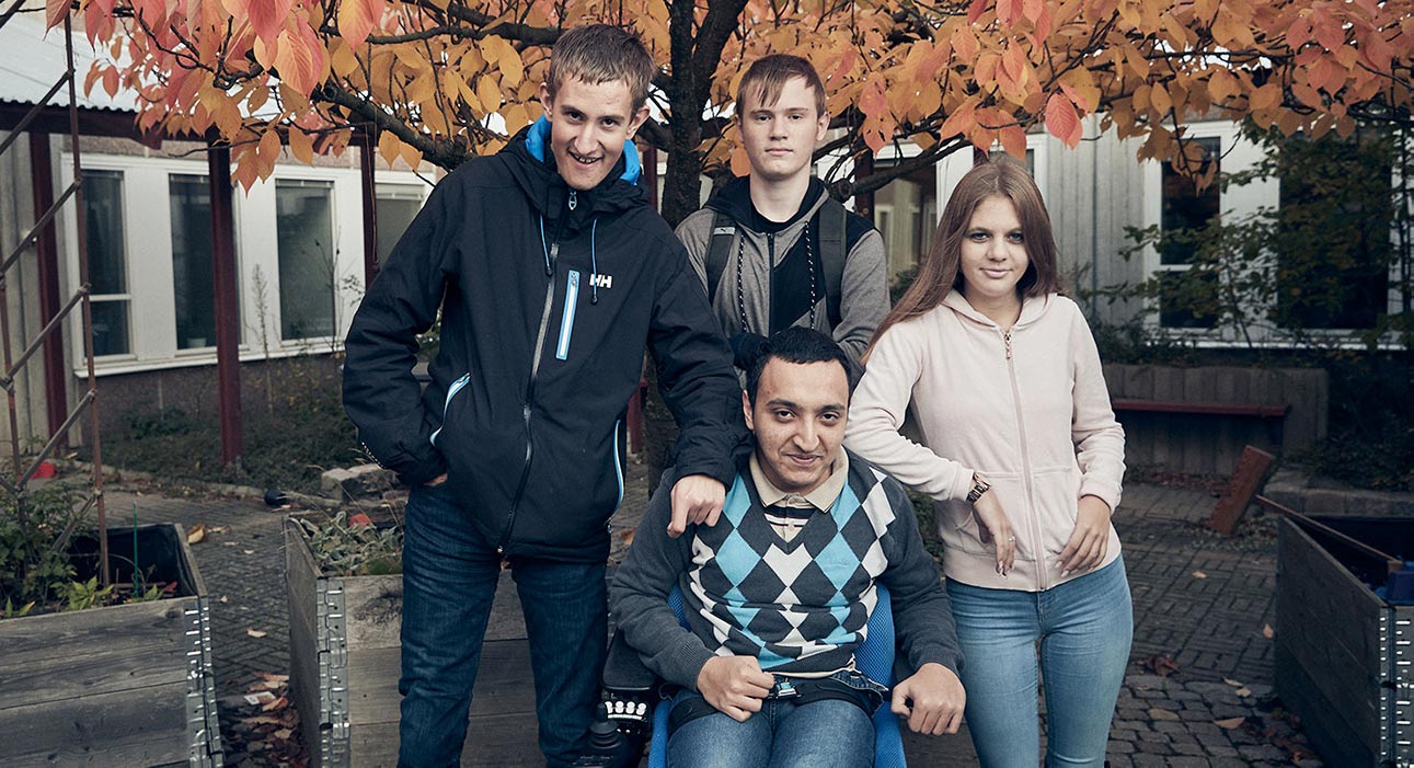 Fyra elever står framför skolan. I bakgrunden finns ett träd med gula löv.