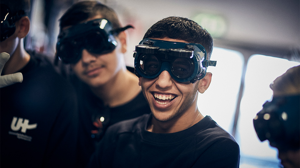 Glad elev med svetsglasögon ser mot kameran.