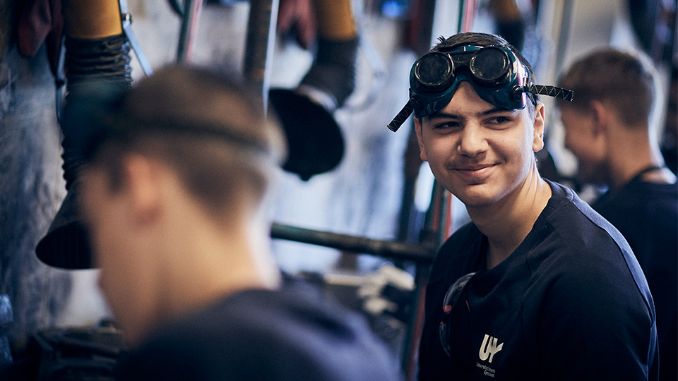 Elev sitter leende bland sina vänner som svetsar.