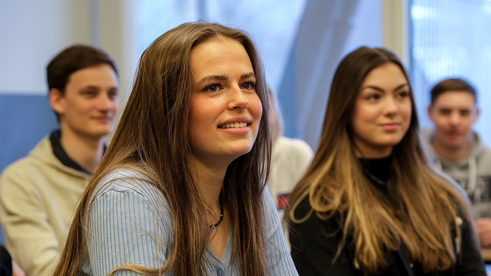 Bild från en lektion. Två leende tjejer i förgrunden och två suddiga killar i bakgrunden.