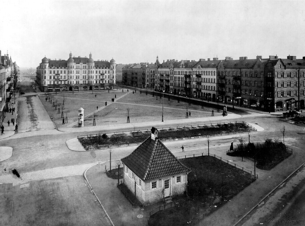 Svartvit bild av ett tomt torg med byggnader runtomkring.