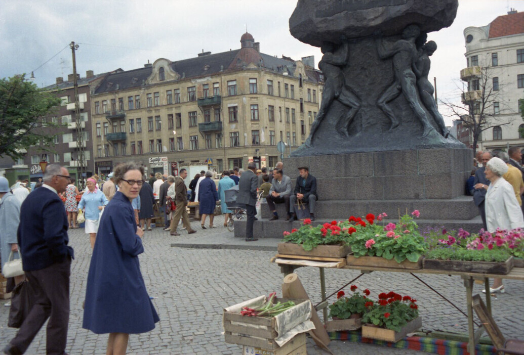 Människor i rörelse över torget vid skulpturen Arbetets ära.